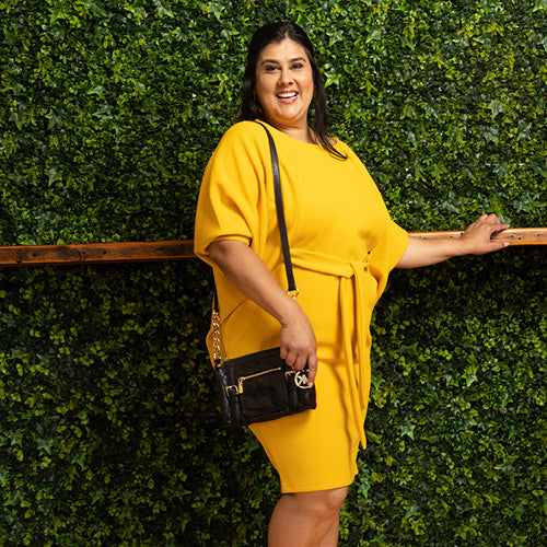 Woman wearing yellow cocktail dress, holding a Michael Kors black crossbody purse.