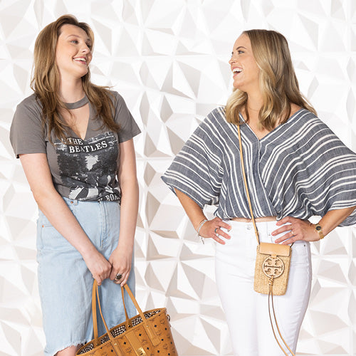 Two Fashionable young adult Women holding designer handbags and wearing spring clothing.